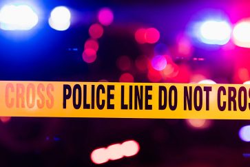 Accident or crime scene cordon tape, police line do not cross. It is nighttime, emergency lights of police cars flashing blue, red and white in the background