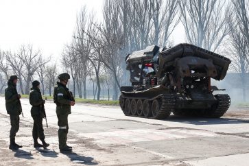 Service members of pro-Russian troops stand next to a combat engineering vehicle, as evacuees board buses to leave the city during Ukraine-Russia conflict in the southern port of Mariupol, Ukraine April 20, 2022. REUTERS/Alexander Ermochenko