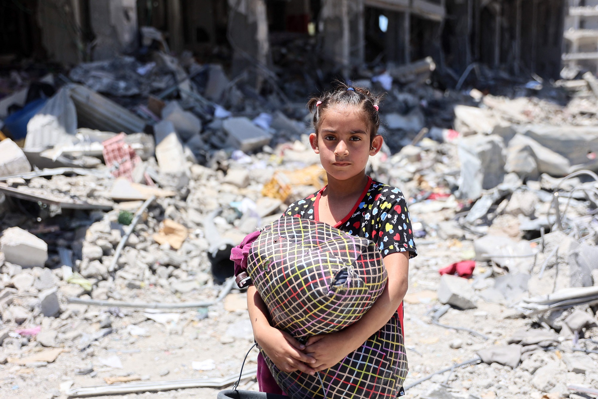 A Palestinian carries some salvaged belongings in the Jabalia refugee camp in the northern Gaza Strip after she returned briefly with others who sought to check on their homes on May 31, 2024, amid the ongoing conflict between Israel and the militant group Hamas. (Photo by Omar AL-QATTAA / AFP)